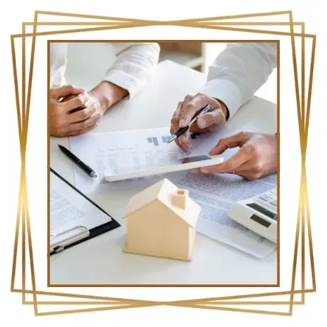 Dos personas revisando documentos, maqueta de una casa sobre una mesa, entorno empresarial.