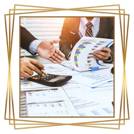 Dos personas vestidas de traje revisando gráficos financieros y usando una calculadora en un escritorio.