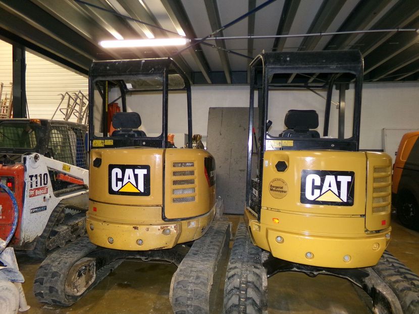 Deux pelles mécaniques CAT jaunes garées côte à côte à l'intérieur d'un entrepôt.