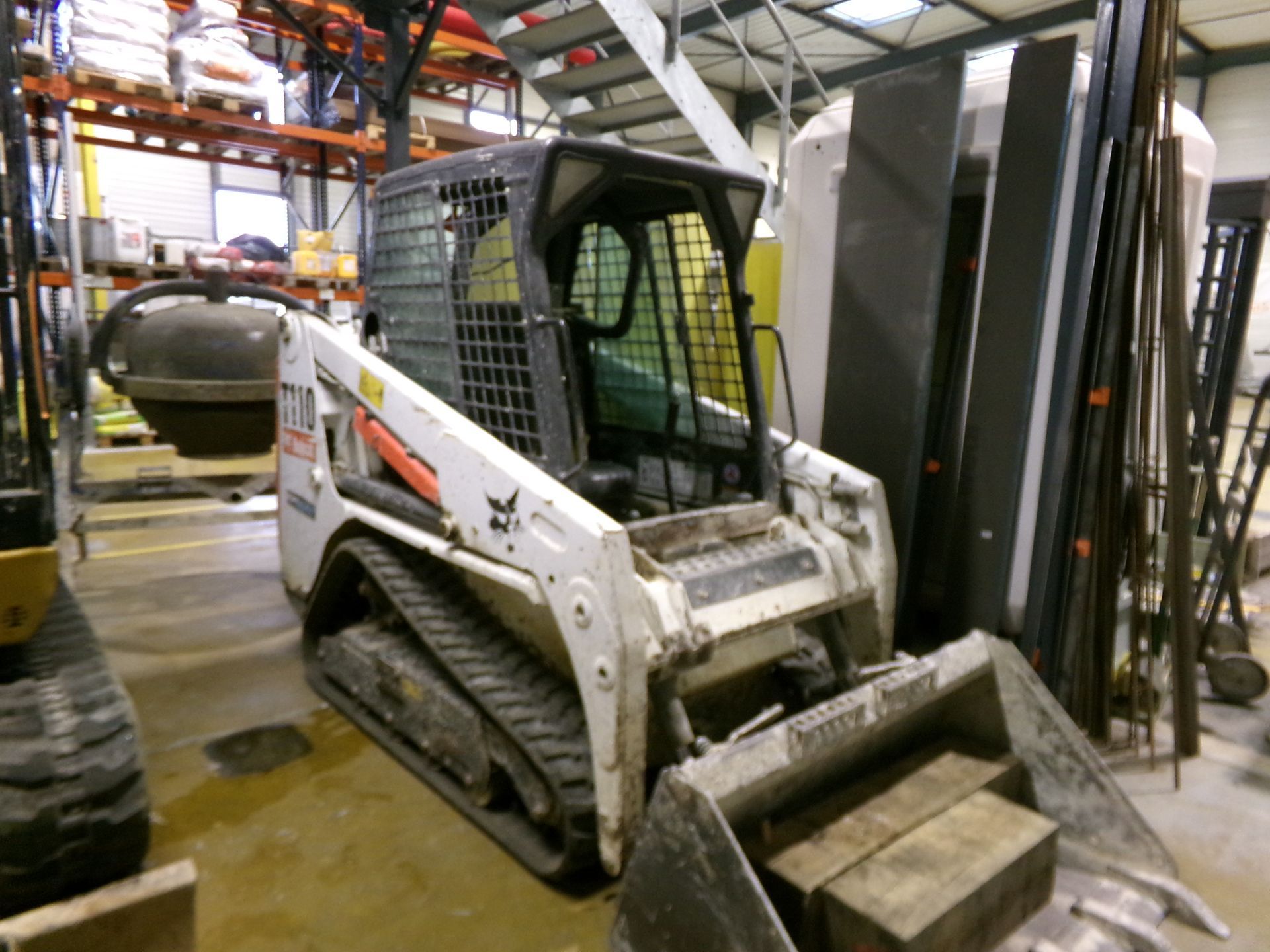 Minichargeuse blanche sur chenilles de marque Bobcat, entreposée dans un hangar.