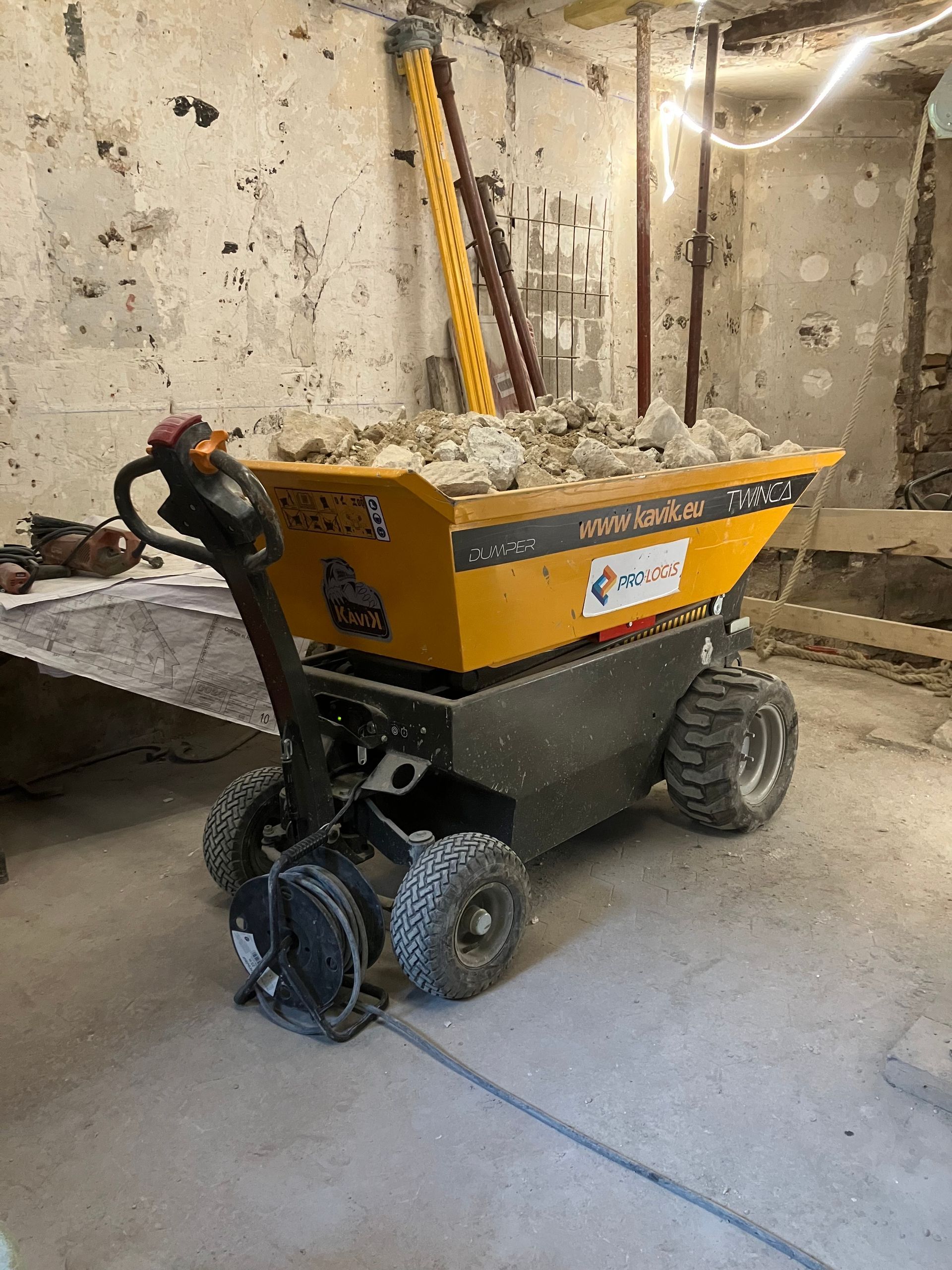 Wagon benne jaune à quatre roues, chargé de pierres, dans un sous-sol en béton.