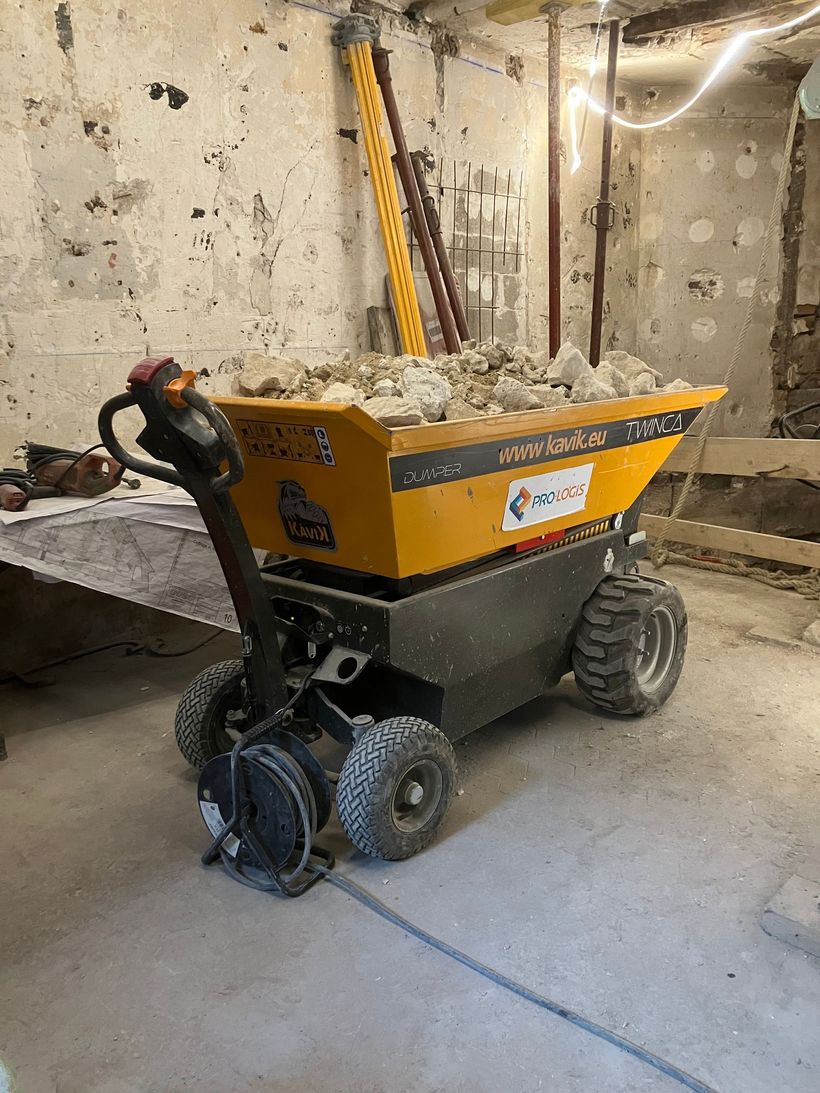 Un wagon benne jaune rempli de gravats est stationné dans une pièce poussiéreuse en béton.