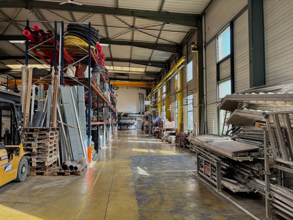 Entrepôt ou hangar industriel avec des échelles empilées, des échafaudages et des rayonnages métalliques.