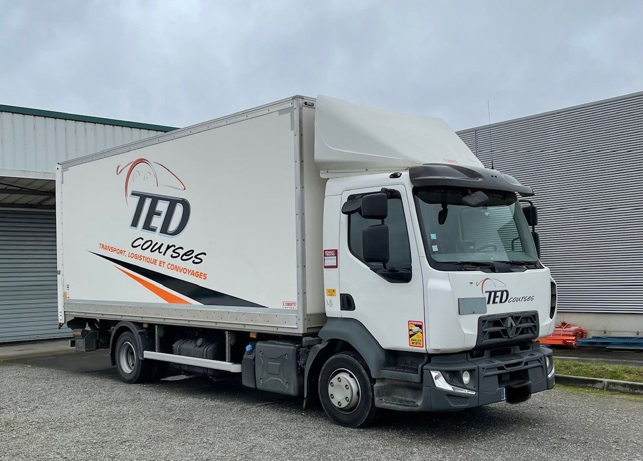 Un camion de livraison blanc TED Crosses est stationné sur du gravier à côté 