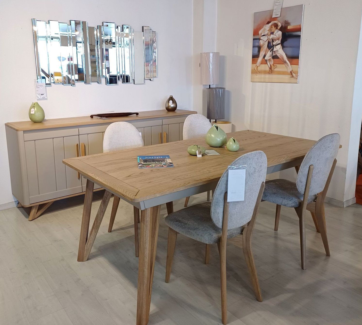 Salle à manger aménagée avec table, chaises, buffet, miroir et éléments de décoration dans une salle d'exposition.