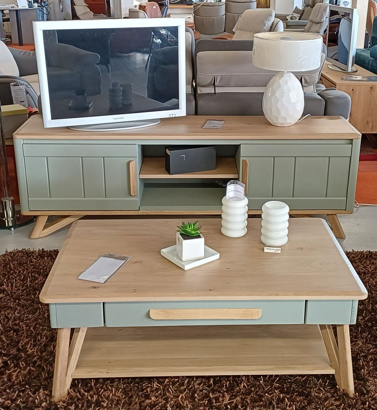 Téléviseur et lampe blanche sur un meuble TV bicolore vert et bois, au-dessus d'une table basse assortie.