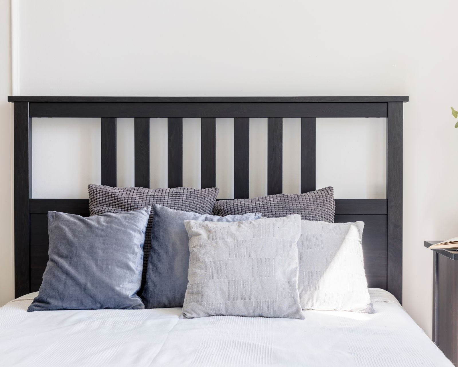 Tête de lit noire et oreillers gris sur un lit aux draps blancs.