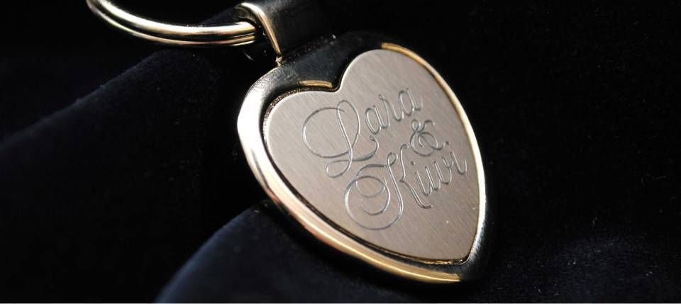 Herzförmiger goldener Schlüsselanhänger mit der eingravierten Aufschrift „Don't Miss“. Vor schwarzem Hintergrund.