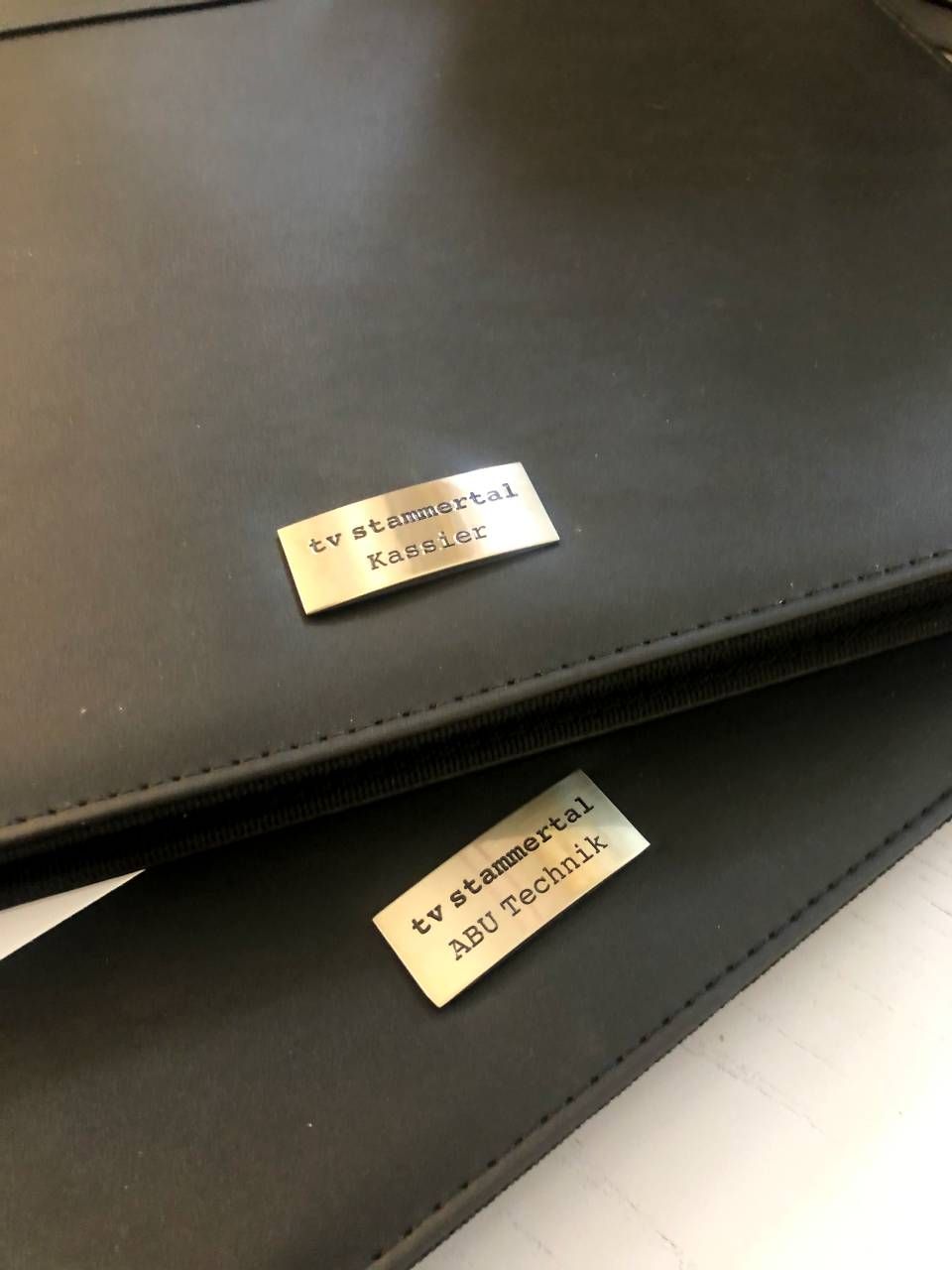 Two black leather portfolios with metal nameplates: 