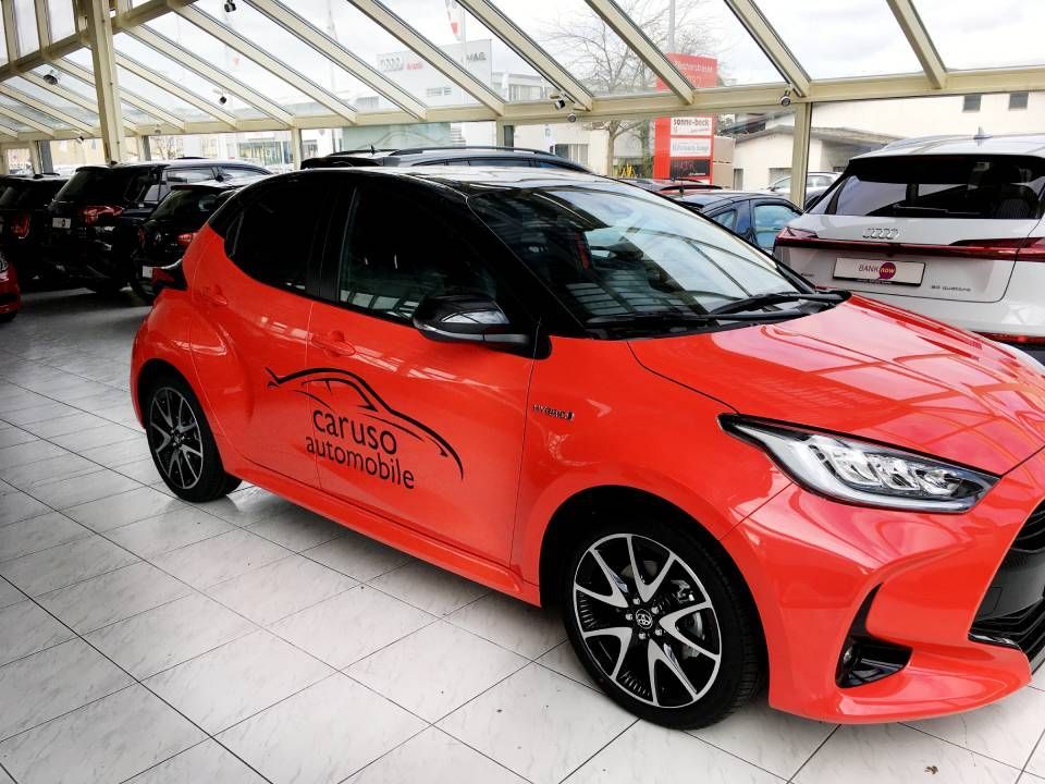 Ein roter Toyota Yaris Hybrid steht im Ausstellungsraum eines Autohauses. Das Logo von „Tarusa Automobile“ prangt an der Tür.