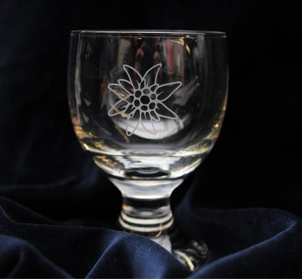 Glas mit geätztem Edelweiss-Blumenmuster, auf einem dunkelblauen Tuch.