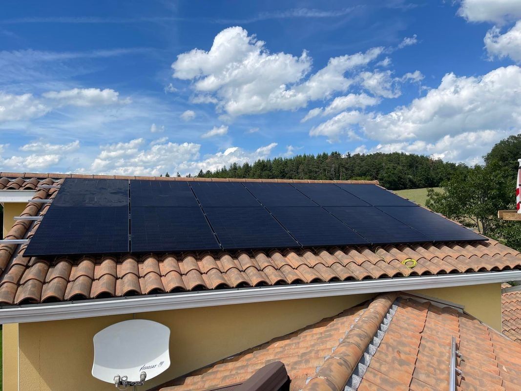 Des panneaux solaires installés sur un toit de tuiles en terre cuite sous un ciel bleu nuageux.