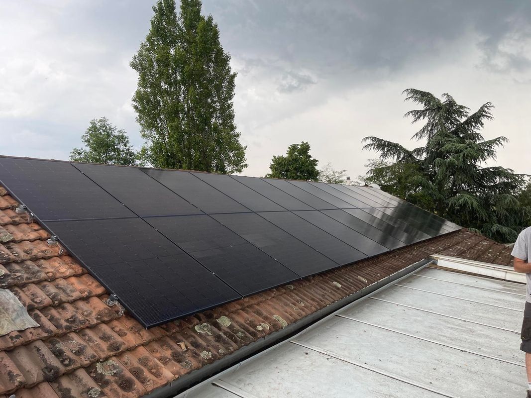 Des panneaux solaires installés sur un toit de tuiles rouges sous un ciel nuageux, avec des arbres en arrière-plan.