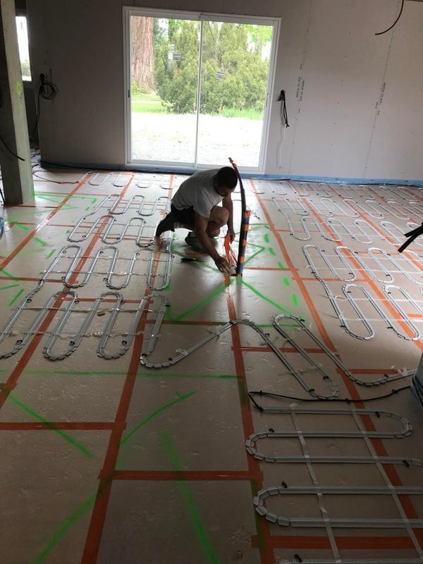 Un homme installe un chauffage au sol radiant, à genoux, à l'aide d'un niveau.