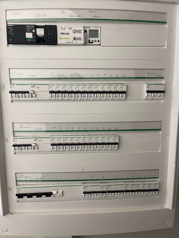 Un électricien teste un tableau électrique avec un multimètre, portant des gants de travail.