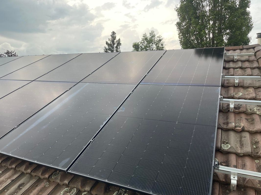 Panneaux solaires installés sur un toit de tuiles à l'aide de supports, sur fond de ciel nuageux.