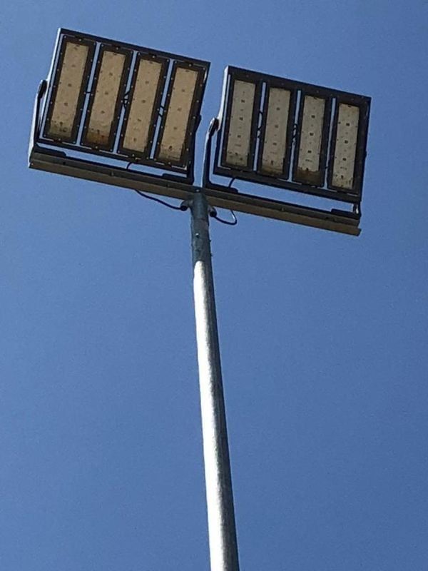 Deux projecteurs LED rectangulaires au sommet d'un grand mât métallique, se détachant sur un ciel bleu.
