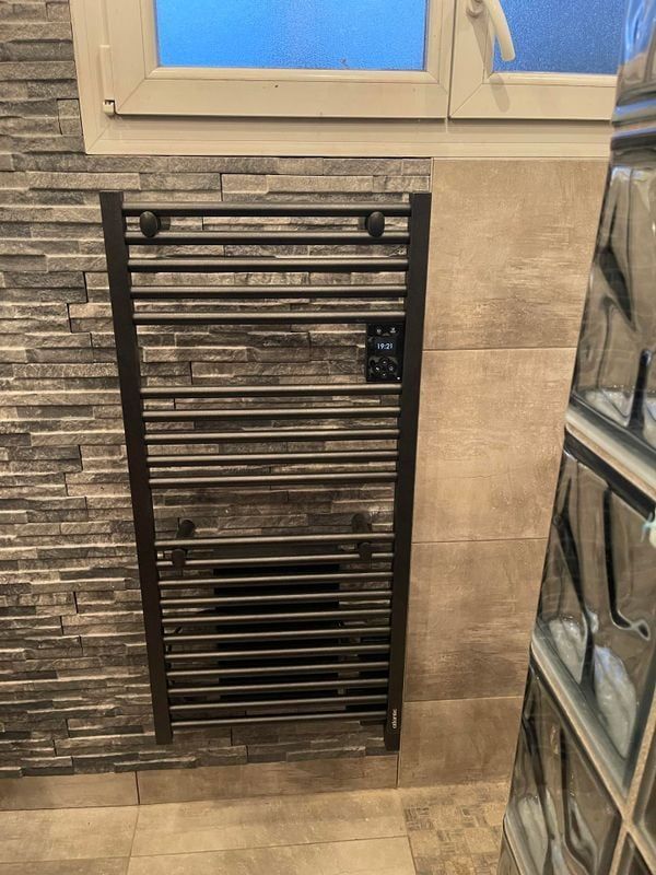 Porte-serviettes chauffant dans une salle de bain, fixé sur un mur carrelé de carreaux gris texturés.