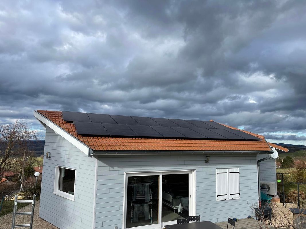 Panneaux solaires sur le toit d'une maison bleu clair sous un ciel nuageux.