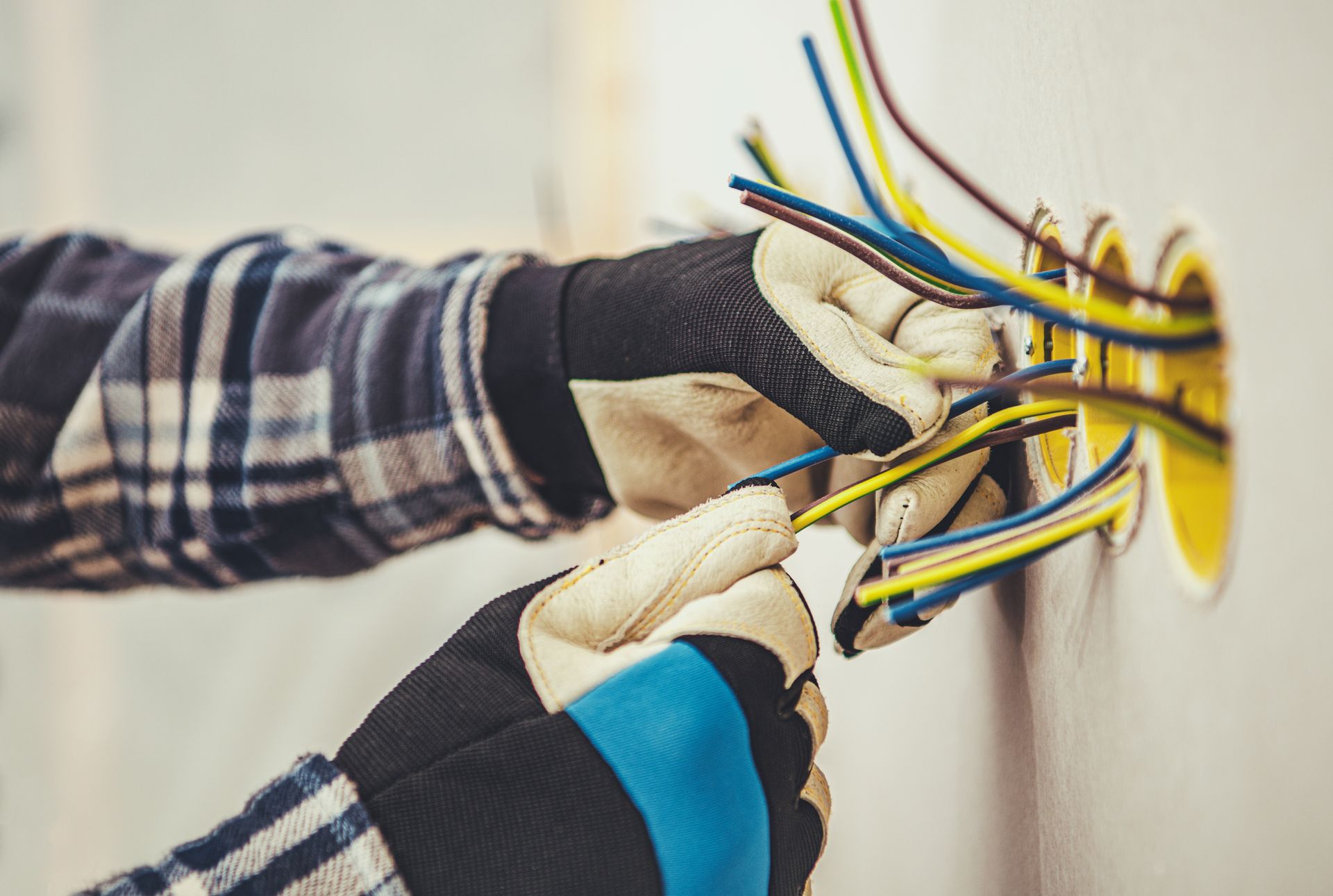 Mains d'électricien gantées connectant des fils à l'intérieur d'un mur. Fils jaunes, bleus et verts.