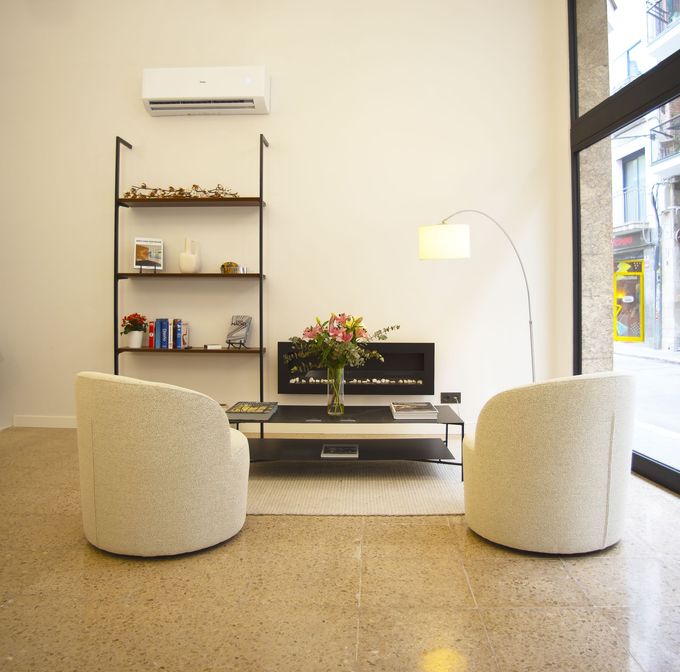 Sala de estar moderna con estantes negros, chimenea, mesa de centro, lámpara de pie y sofá beige. Oficina Sitges Barcelona. Agencia Inmobiliaria.