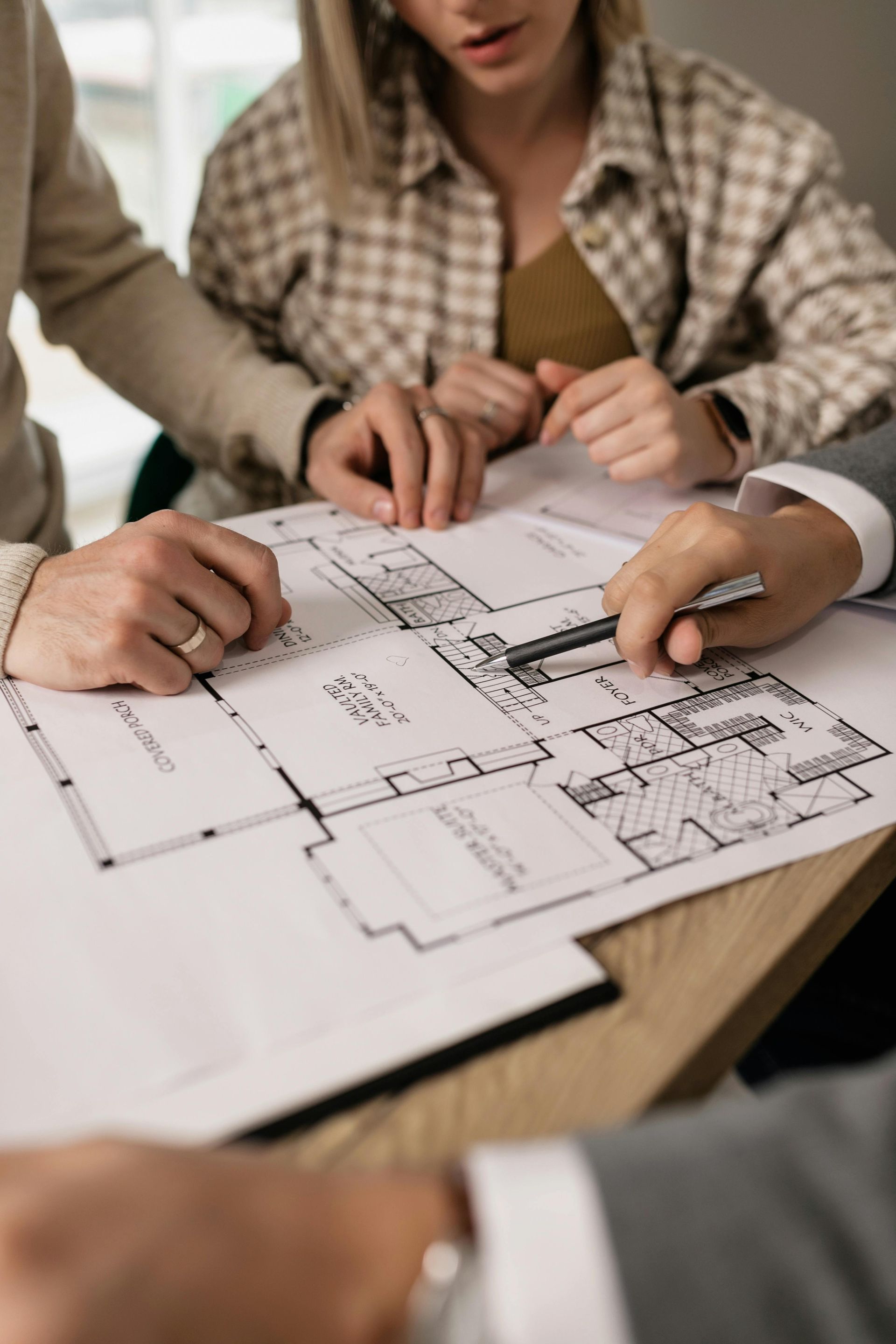 Manos señalando planos arquitectónicos sobre una mesa con un lápiz de dibujo cerca