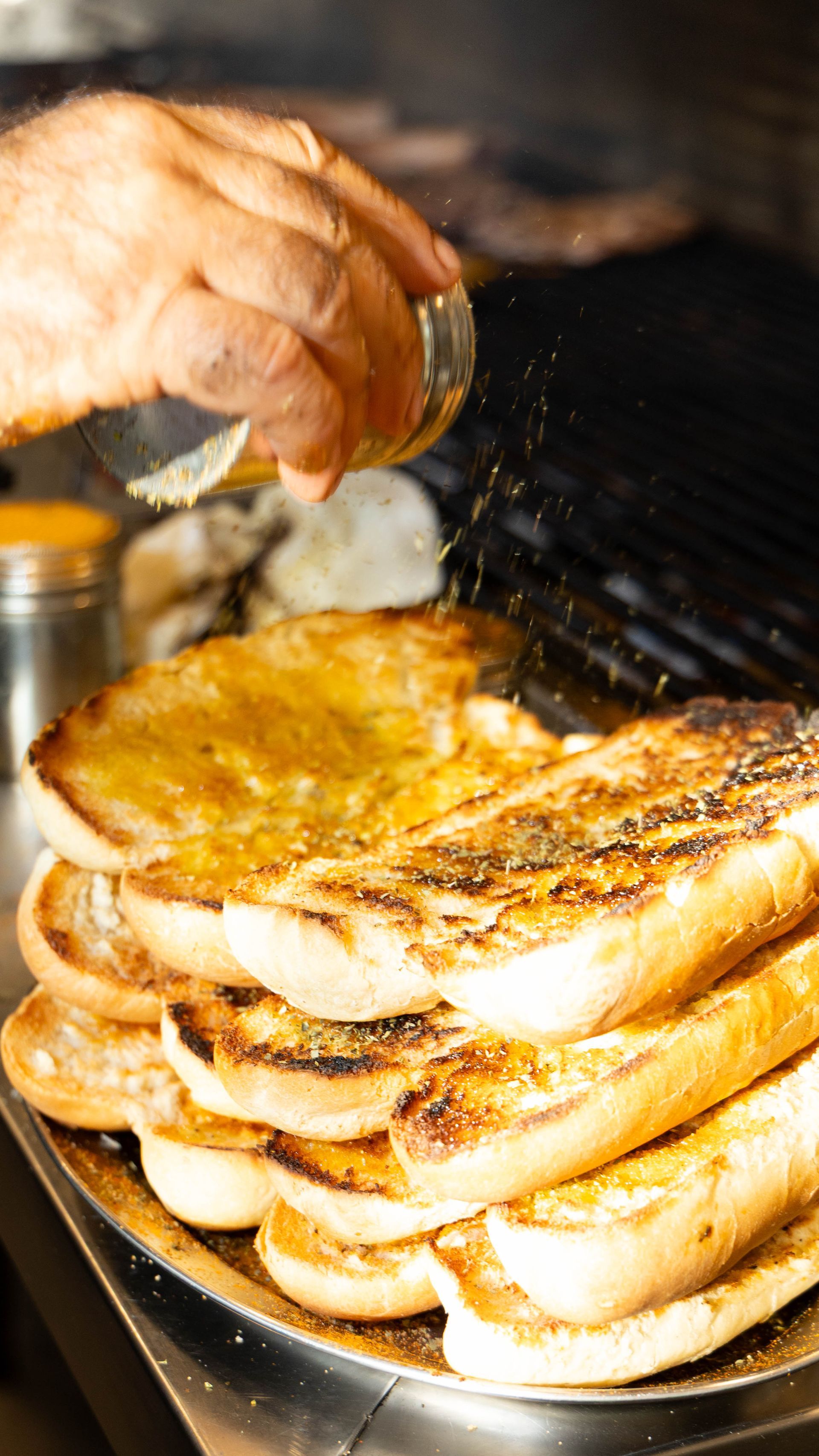 Ράντισμα καρυκευμάτων με το χέρι σε μια στοίβα ψητού ψωμιού σε μεταλλική πιατέλα.