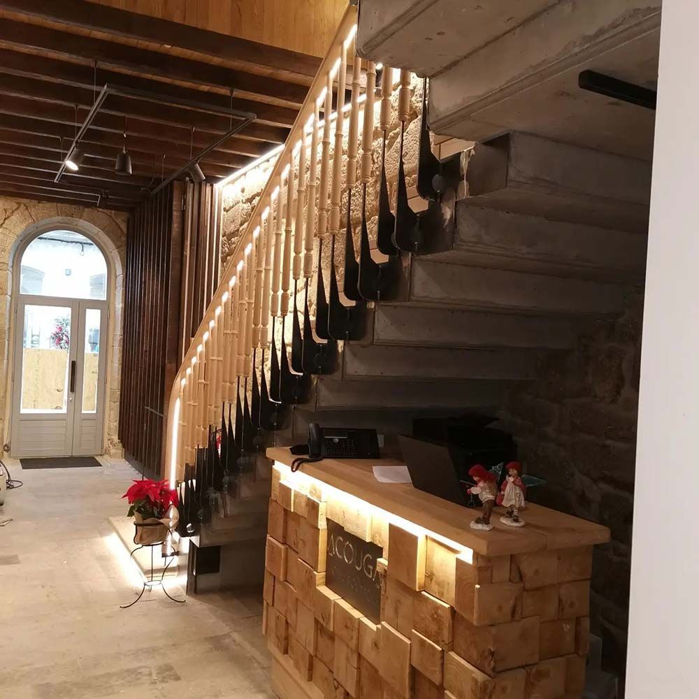 Recepción con escritorio de madera y escalera con una barandilla única. Se ven paredes de piedra y una puerta.