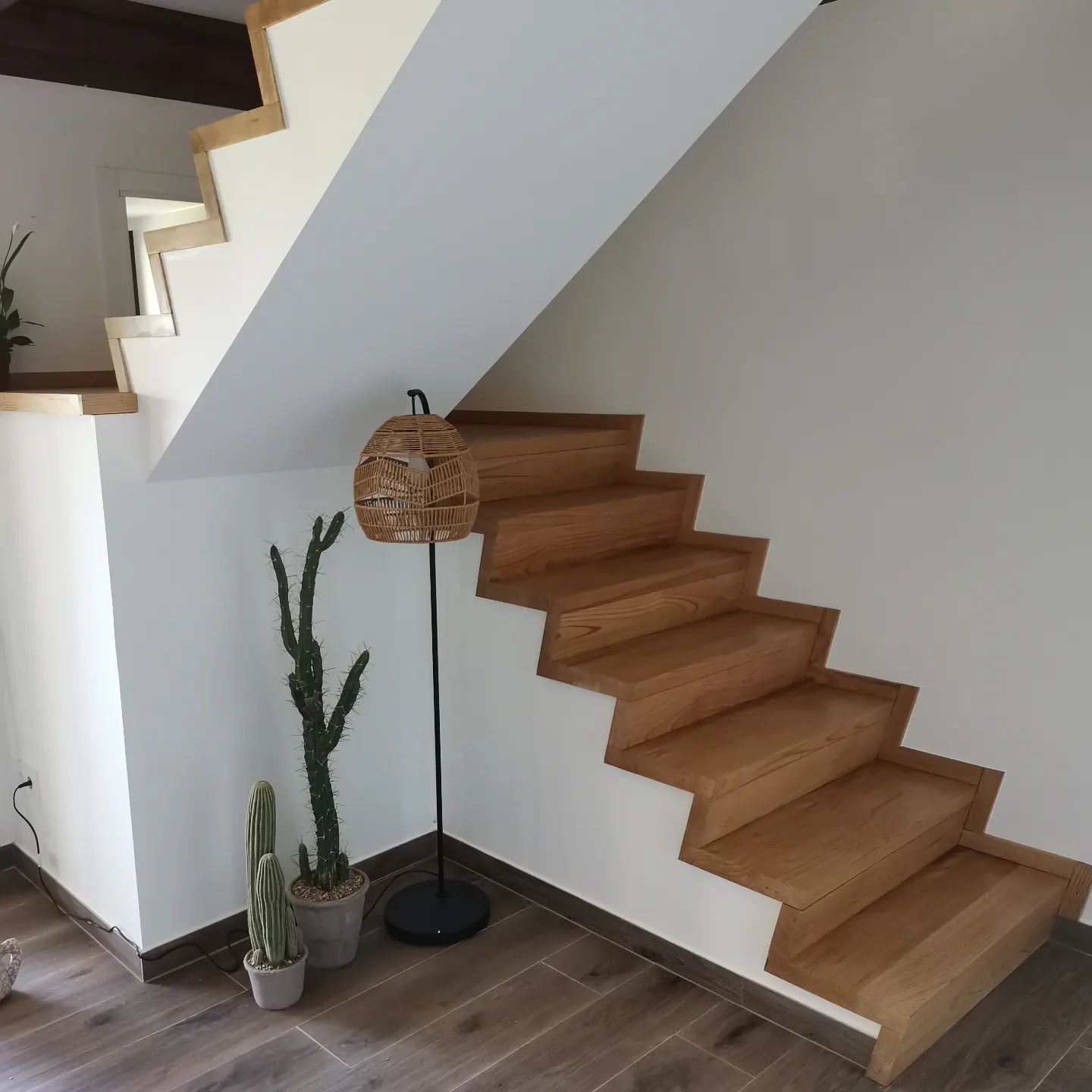 Escalera de madera con paredes blancas, lámpara de pie y plantas en macetas.