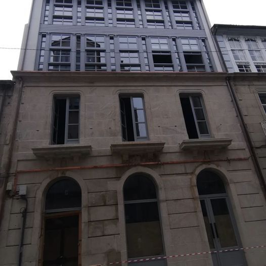 Fachada de edificio con plantas inferiores de piedra y plantas superiores de metal moderno, ventanas en todas partes.