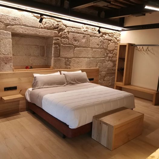 Dormitorio con pared de piedra, cama, muebles de madera.