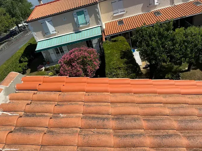 Toit en tuiles orange, vue sur des maisons avec auvent turquoise et arbustes.