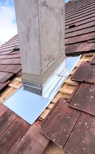 Cheminée sur un toit de tuiles avec solins, montrant des travaux de réparation de toiture.