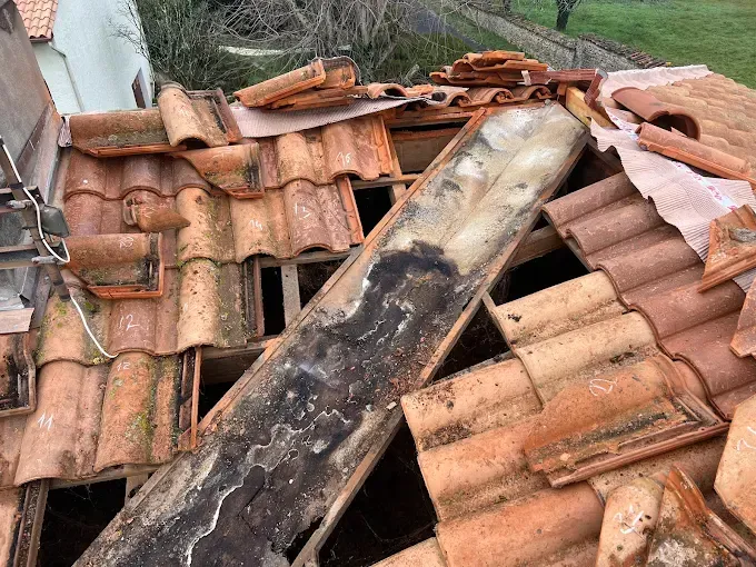 Toiture endommagée, tuiles manquantes et poutres en bois apparentes.