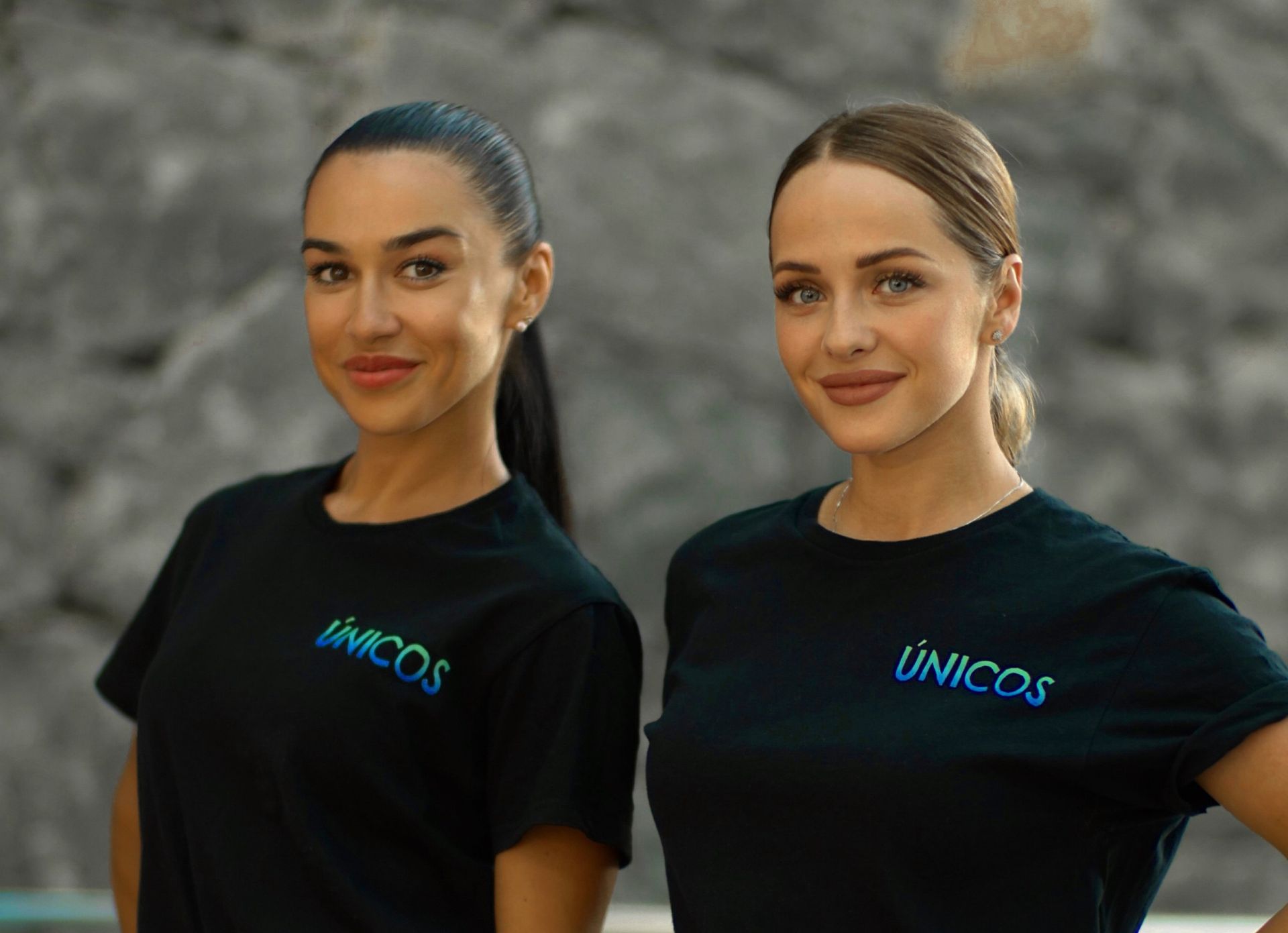 Dos mujeres que llevan camisetas negras con la palabra Unicos escritas en ellas están paradas una al lado de la otra.