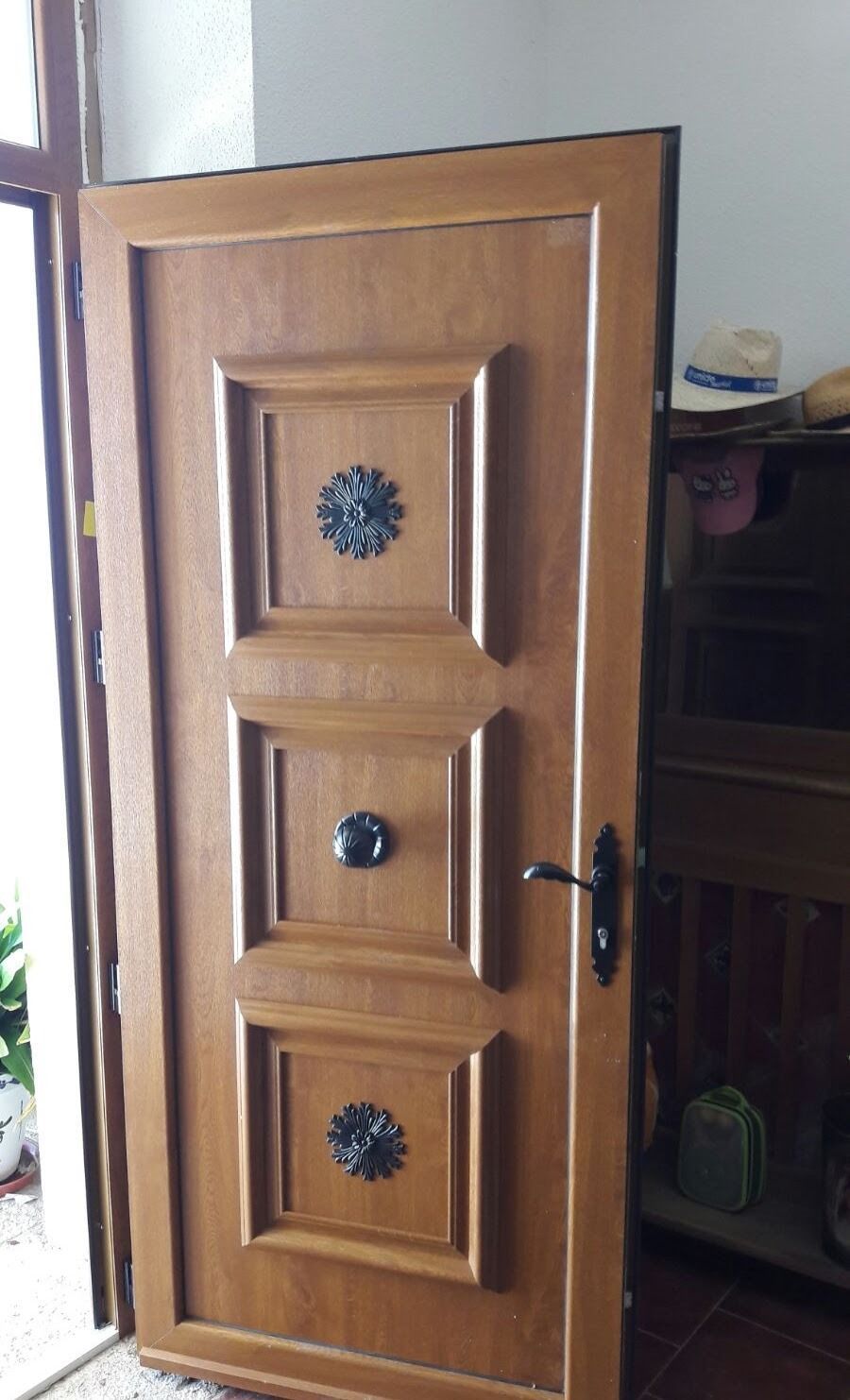 Puerta principal de madera con paneles decorativos, ligeramente abierta, que deja ver una habitación interior con poca luz.