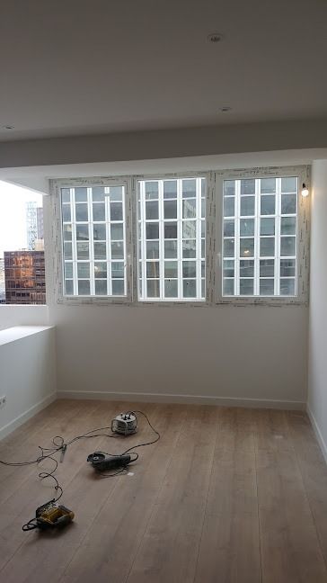 Habitación vacía con suelo de madera clara, paredes blancas y una gran ventana al fondo.