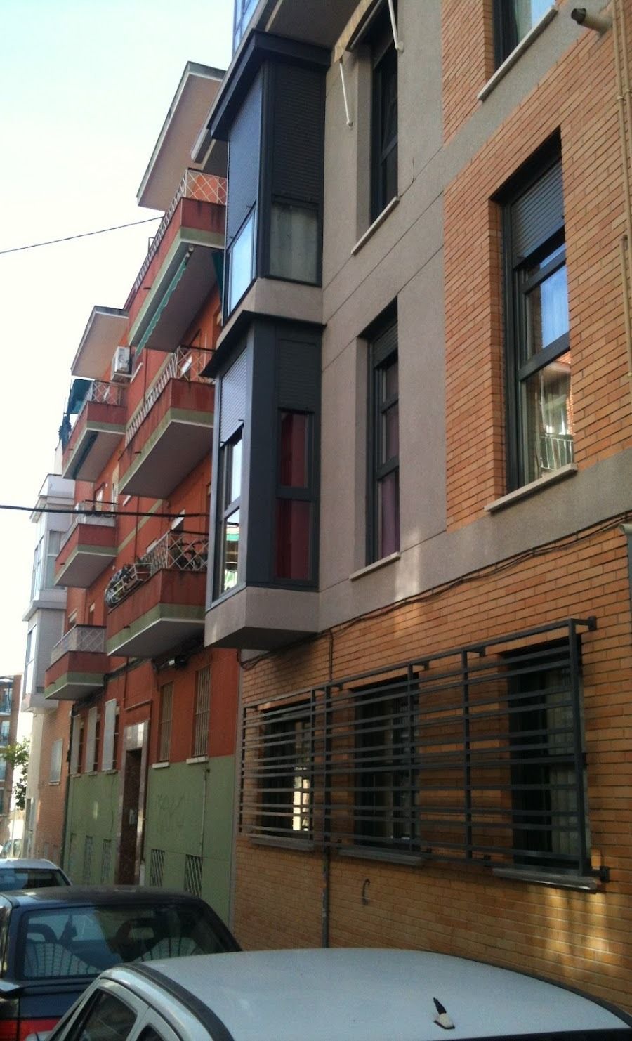 Calle estrecha flanqueada por edificios de apartamentos de ladrillo y balcones, con coches aparcados debajo.