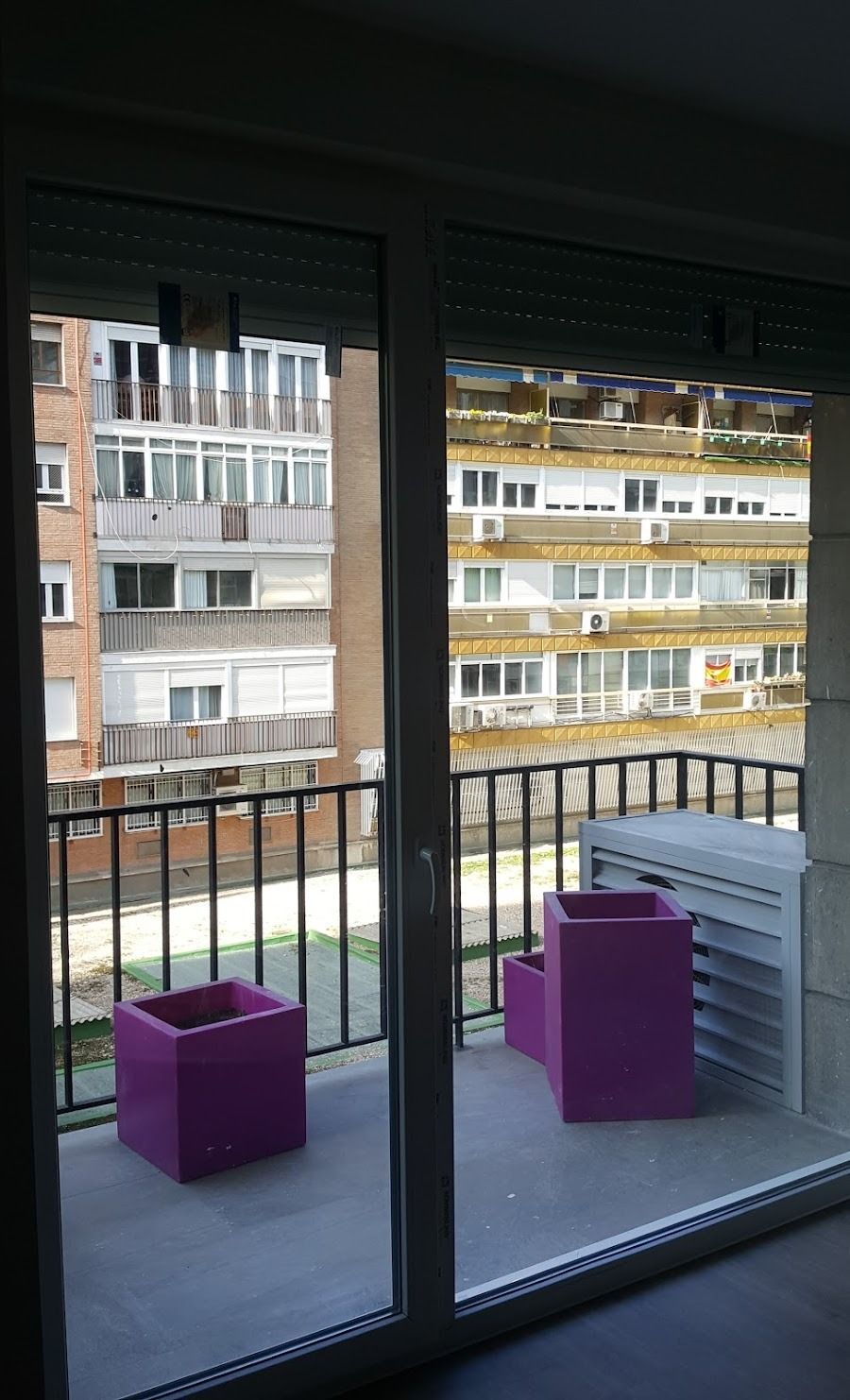 Balcón con dos asientos cúbicos morados con vistas a los edificios de apartamentos a través de puertas corredizas de cristal.