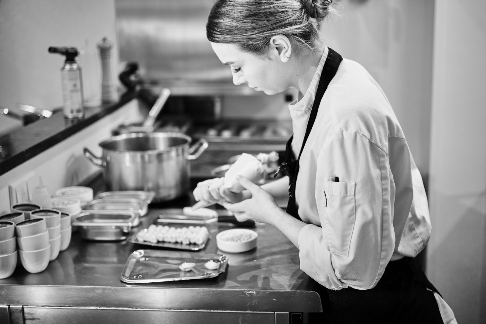 Op een zwart-witfoto is een vrouw bezig met het bereiden van eten in de keuken.