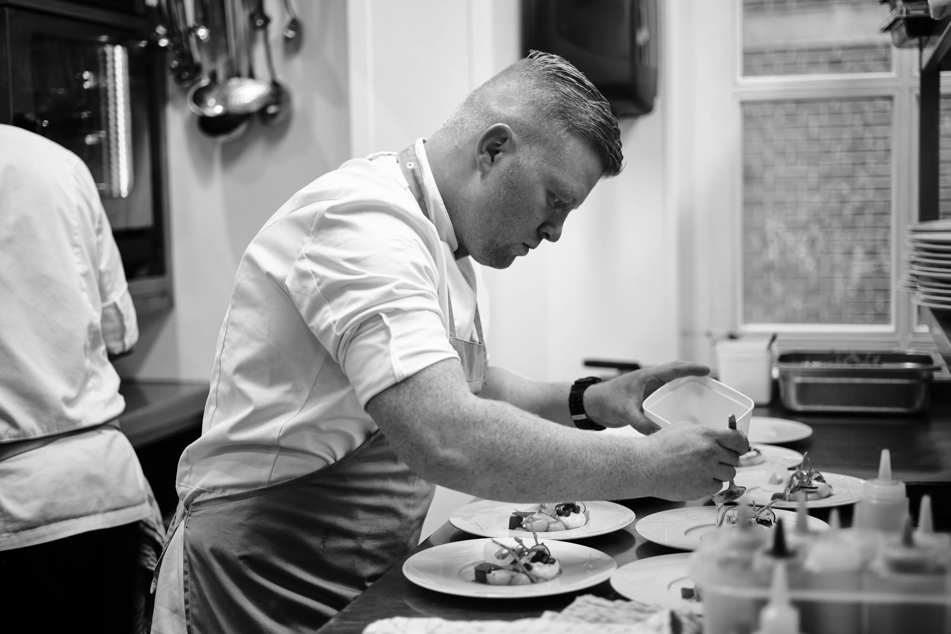 Een zwart-witfoto van een chef-kok die eten bereidt in een keuken.