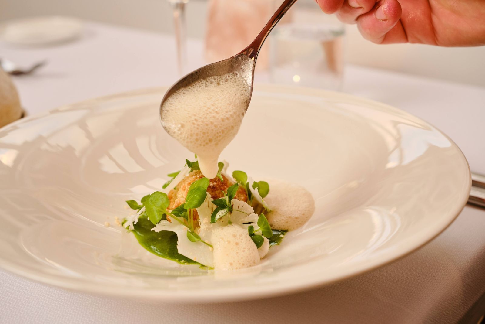 Iemand giet met een lepel saus op een bord eten.