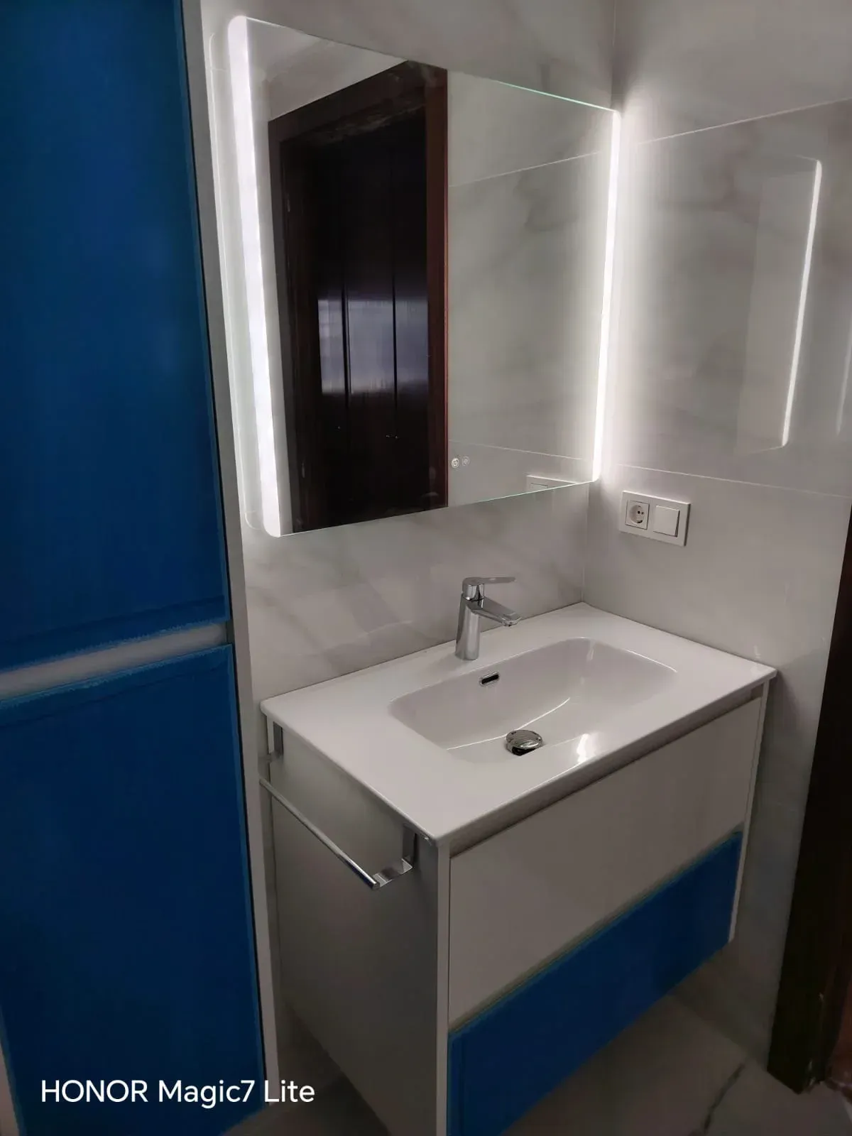 Mueble de baño moderno con espejo, lavabo blanco, grifo cromado y pared azul de acento.