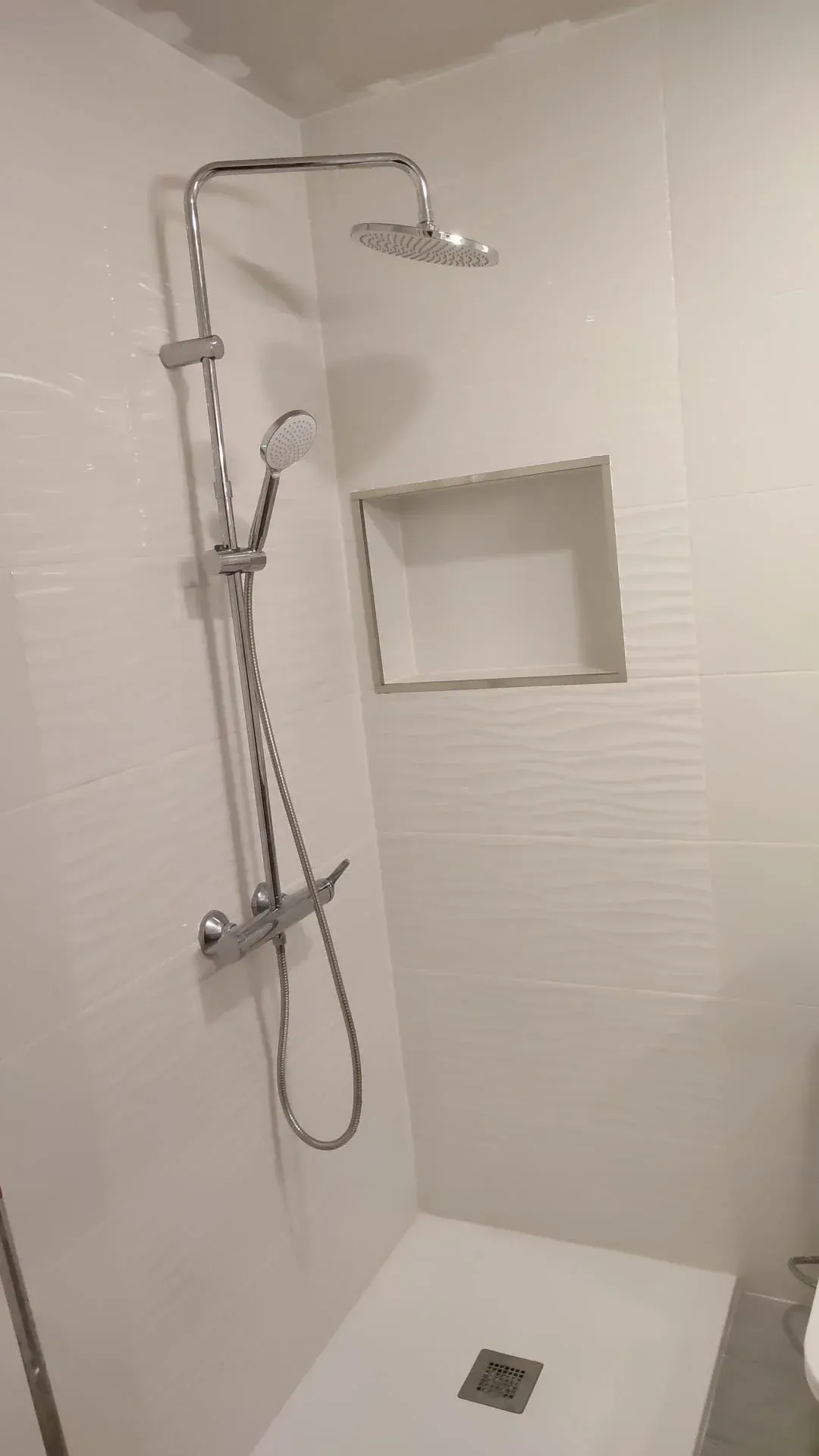 Ducha a ras de suelo accesible con ducha de mano, barra de apoyo y nicho empotrado en un baño alicatado en blanco