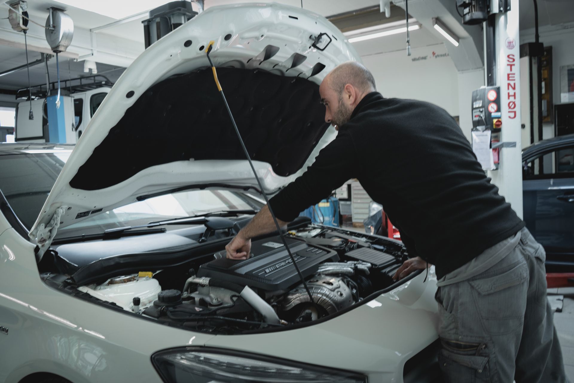 Un mécanicien travaille sur le moteur d'une voiture tout en tenant un presse-papiers.