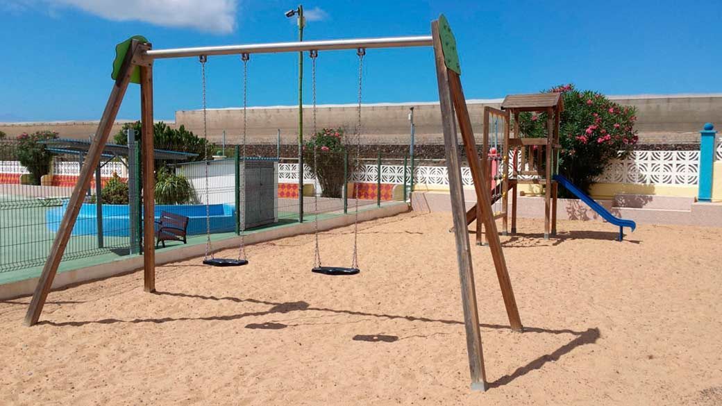 Un parque infantil con columpios y un tobogán en la arena.