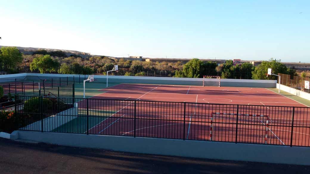 Una cancha de tenis con una valla alrededor y árboles al fondo.