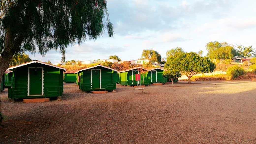 Una hilera de casas verdes se encuentran encima de un campo de tierra.