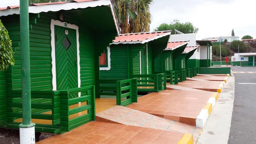 Una hilera de cabañas de madera verdes están alineadas al costado del camino.