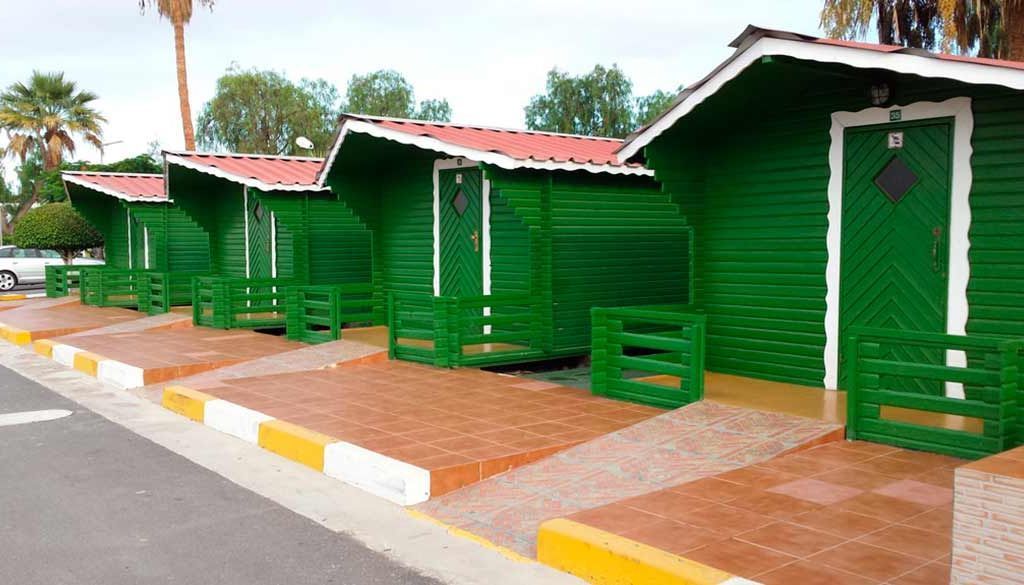 Una hilera de casas verdes están alineadas una al lado de la otra al costado de la carretera.